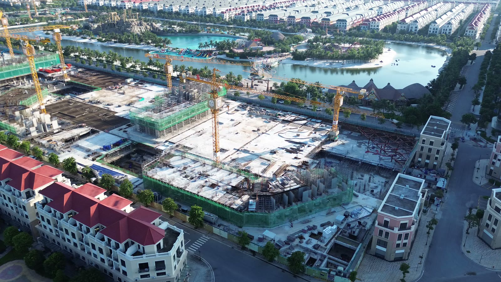 Công trường Masteri Grand Coast nhìn từ trên cao, phía sau là hồ tạo sóng và bãi cát, phía trước là dãy nhà thấp tầng mái đỏ và đường nội khu Ocean Park