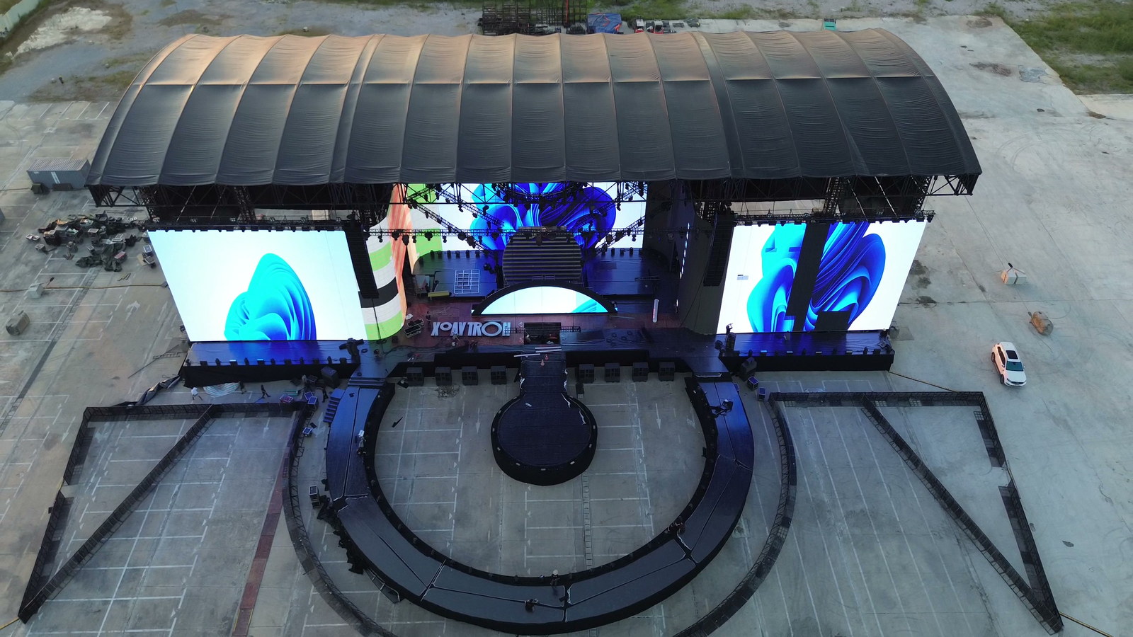 Sân khấu tròn của concert Xoay Tròn nhìn từ flycam, mái cong bằng kim loại che ba màn hình LED lớn đang phát hình xoáy màu xanh, phía trước là sàn tròn và các lối đi hình nan quạt